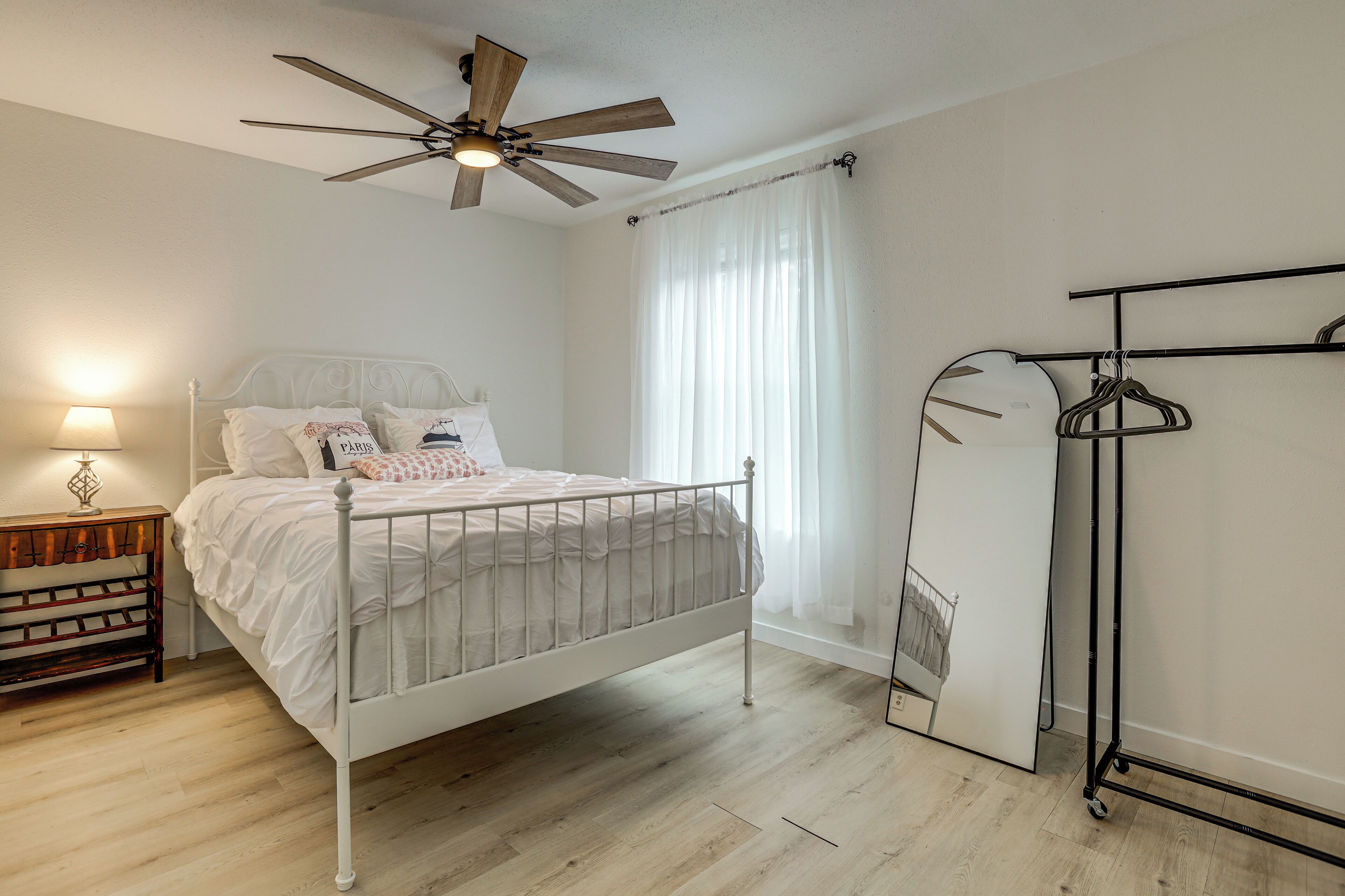 Quarto com cama, ventoinha no teto, mesa de cabeceira com abajur e guarda-roupa.