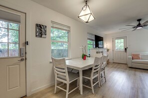 Un espace repas avec une table et des chaises blanches, un ventilateur de plafond et une vue sur l’extérieur.