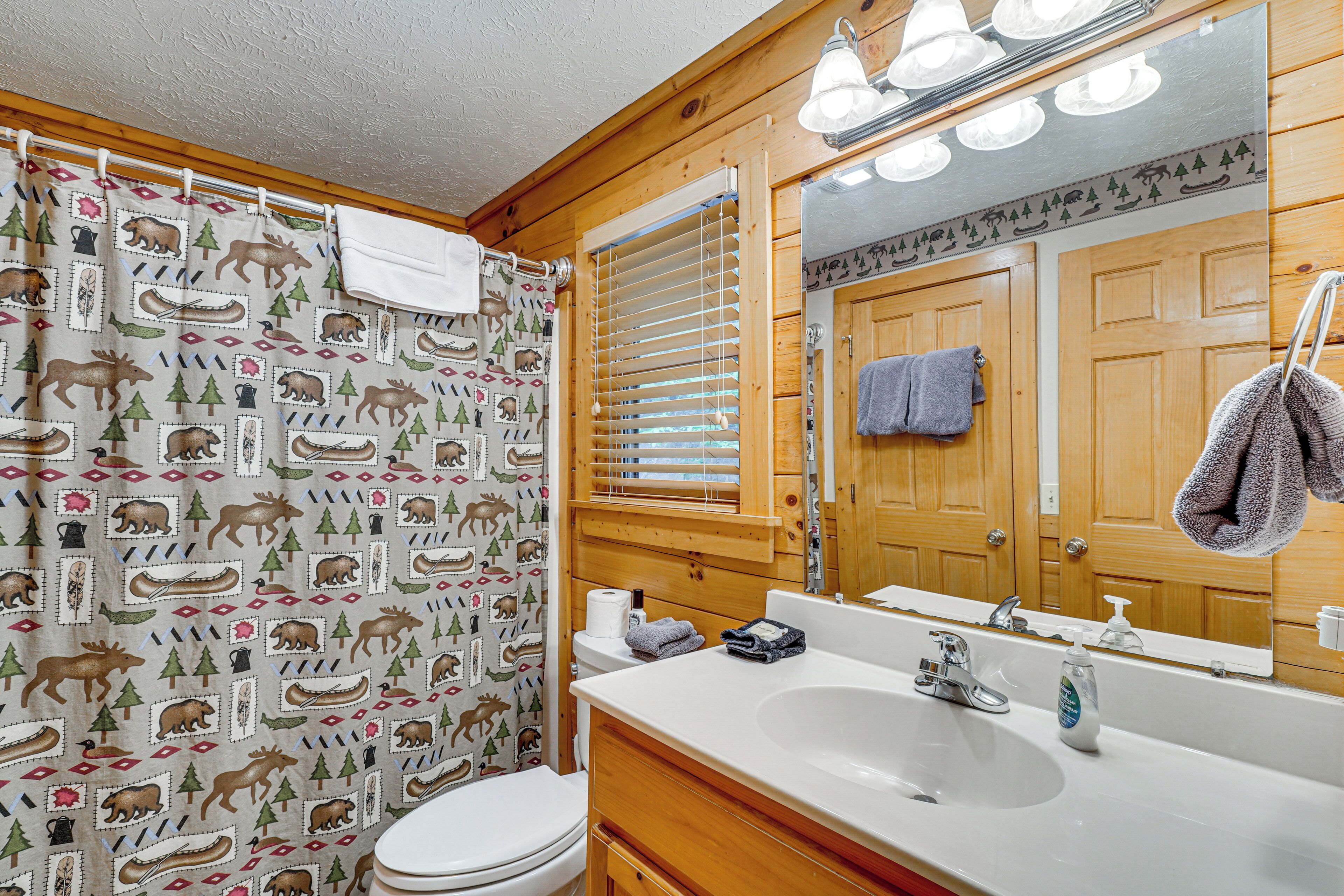 A bathroom with a wooden interior, a white sink, a mirror, and a shower curtain with animal prints.