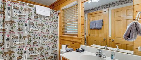 A bathroom with a wooden interior, a white sink, a mirror, and a shower curtain with animal prints.
