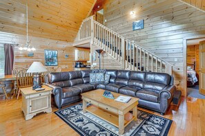 Ein Holzinnenraum mit Ledersofa, einem Holztisch, einer Treppe und einem Essbereich mit Stühlen und Tisch.
