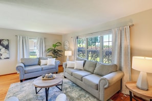 A living room with two sofas, a coffee table, a lamp, a clock, and a window with curtains. - Great for Families! Omaha Getaway w/ Yard & Deck (Omaha)
