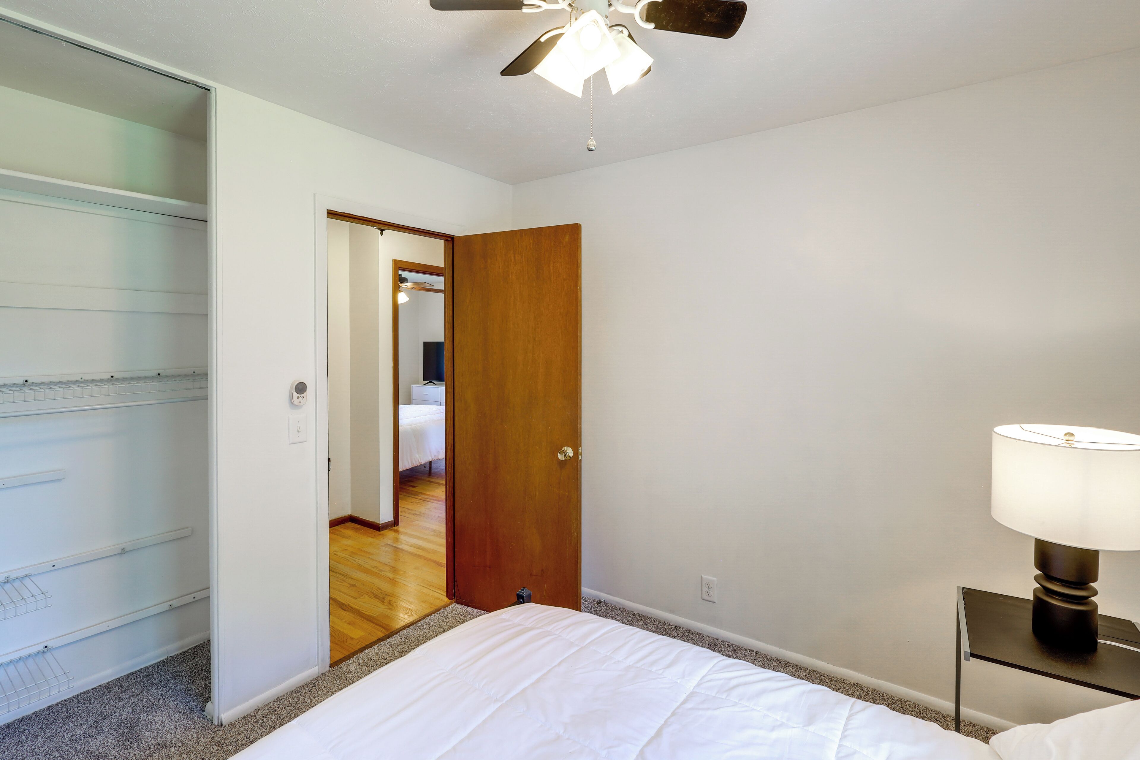 Una camera da letto con un letto, un comodino con una lampada, una ventola a soffitto e un armadio.