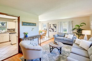 A living room with a sofa, armchair, and coffee table, a dining area with a table and chairs, and a kitchen with cabinets and a window. - Great for Families! Omaha Getaway w/ Yard & Deck (Omaha)
