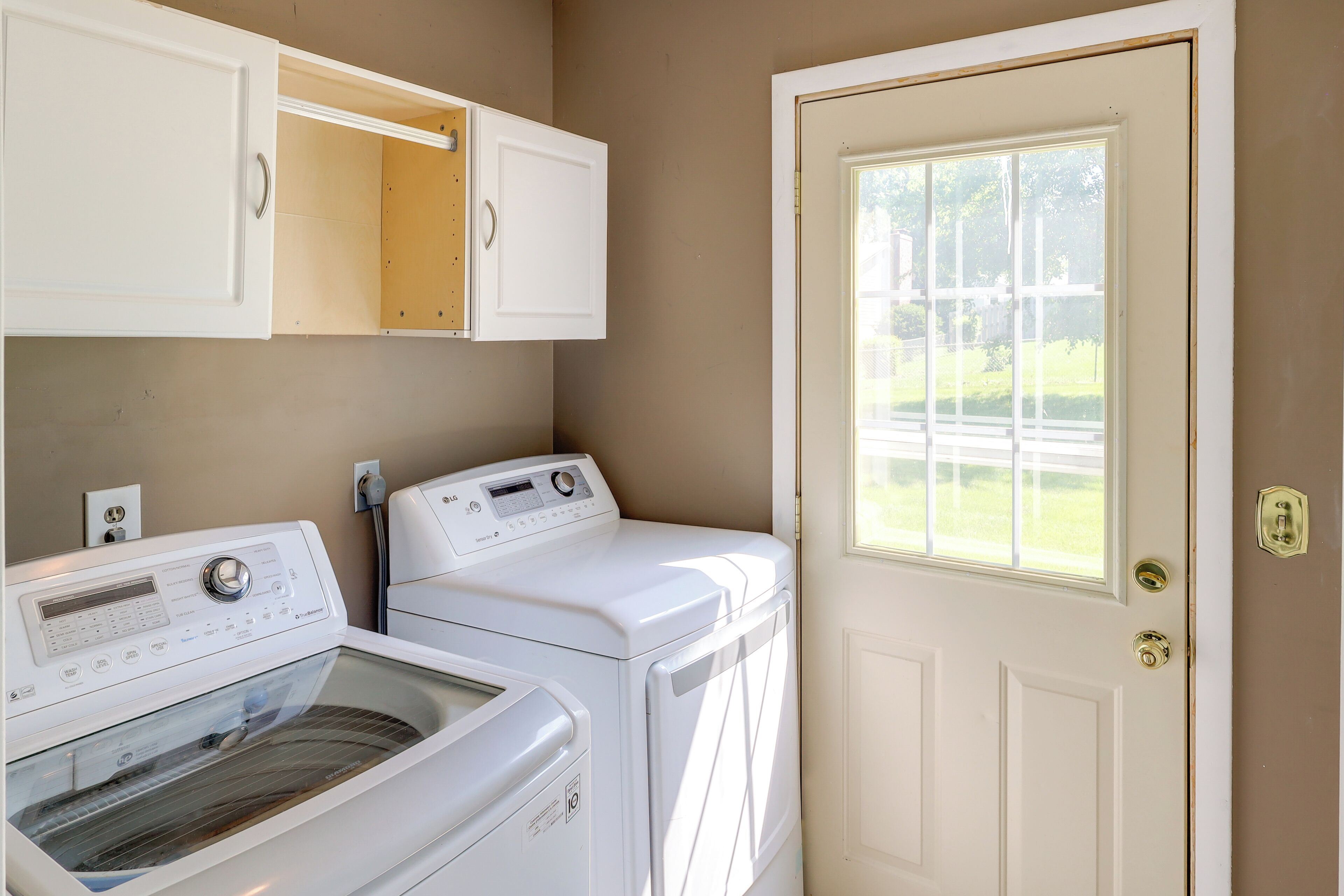 A laundry room with two front-loading washers and dryers, a cabinet above the dryers, and a door with a window.
