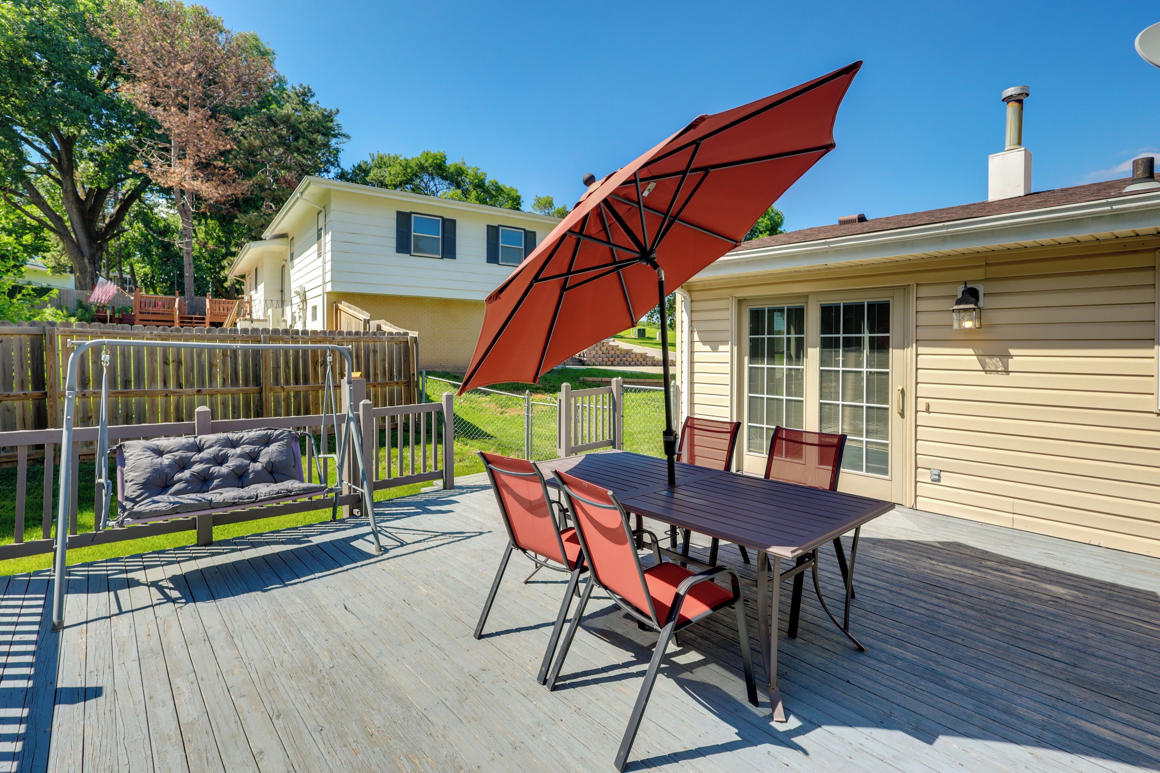 A deck with a table and chairs, a swing, and a red umbrella.