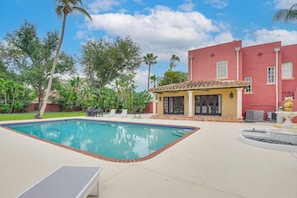 A swimming pool with a tiled edge, a patio area with lounge chairs, and a building with a red facade and tiled roof. - 5 Mi to Anna Maria Island! Family Getaway w/ Pool (Bradenton)