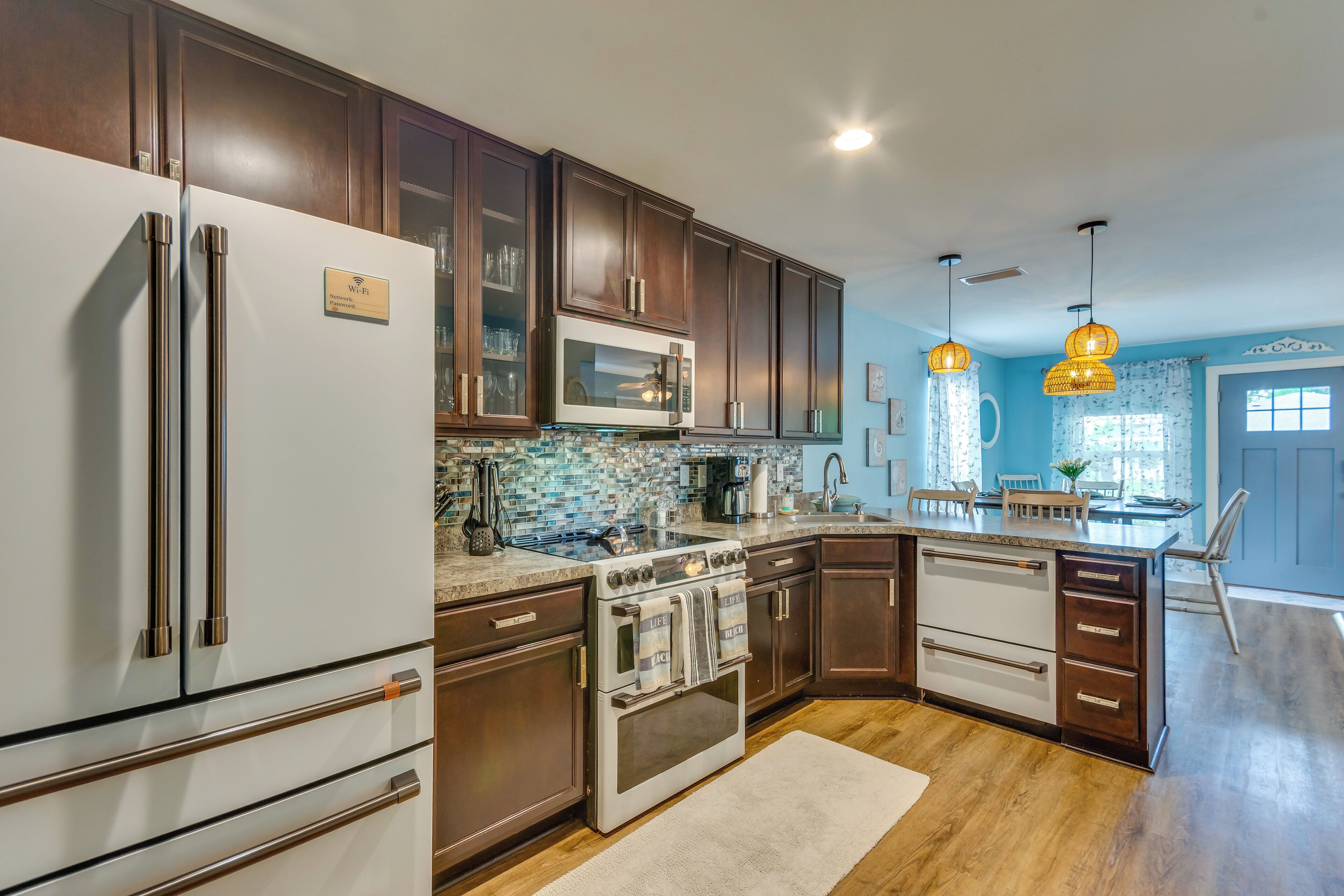 A kitchen with dark wood cabinets, stainless steel appliances, a tiled backsplash, and pendant lighting.