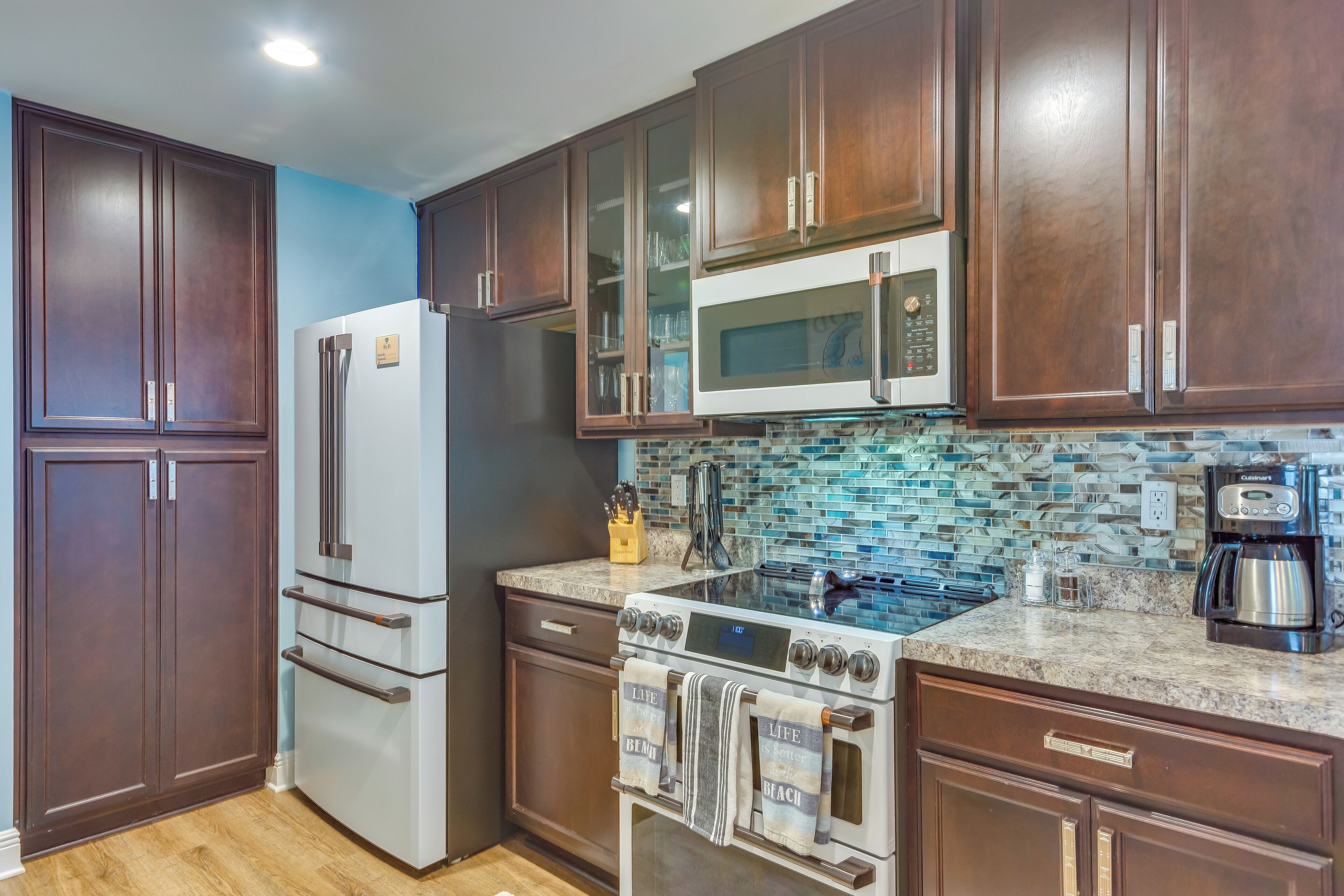 A kitchen with dark wooden cabinets, a stainless steel refrigerator, a microwave, a stove, and a coffee maker.