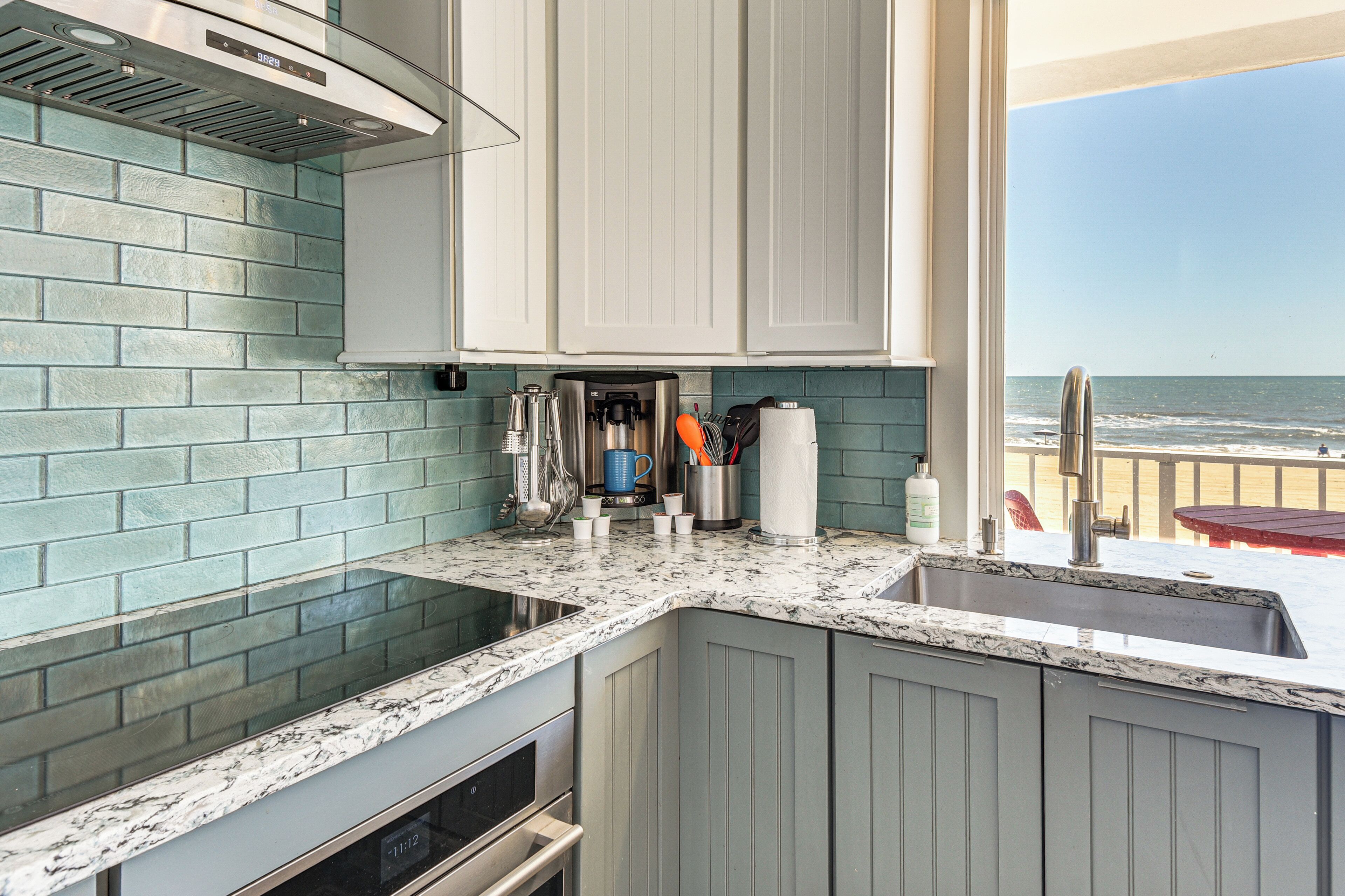 A kitchen with a view of the ocean, a sink, and a stove.