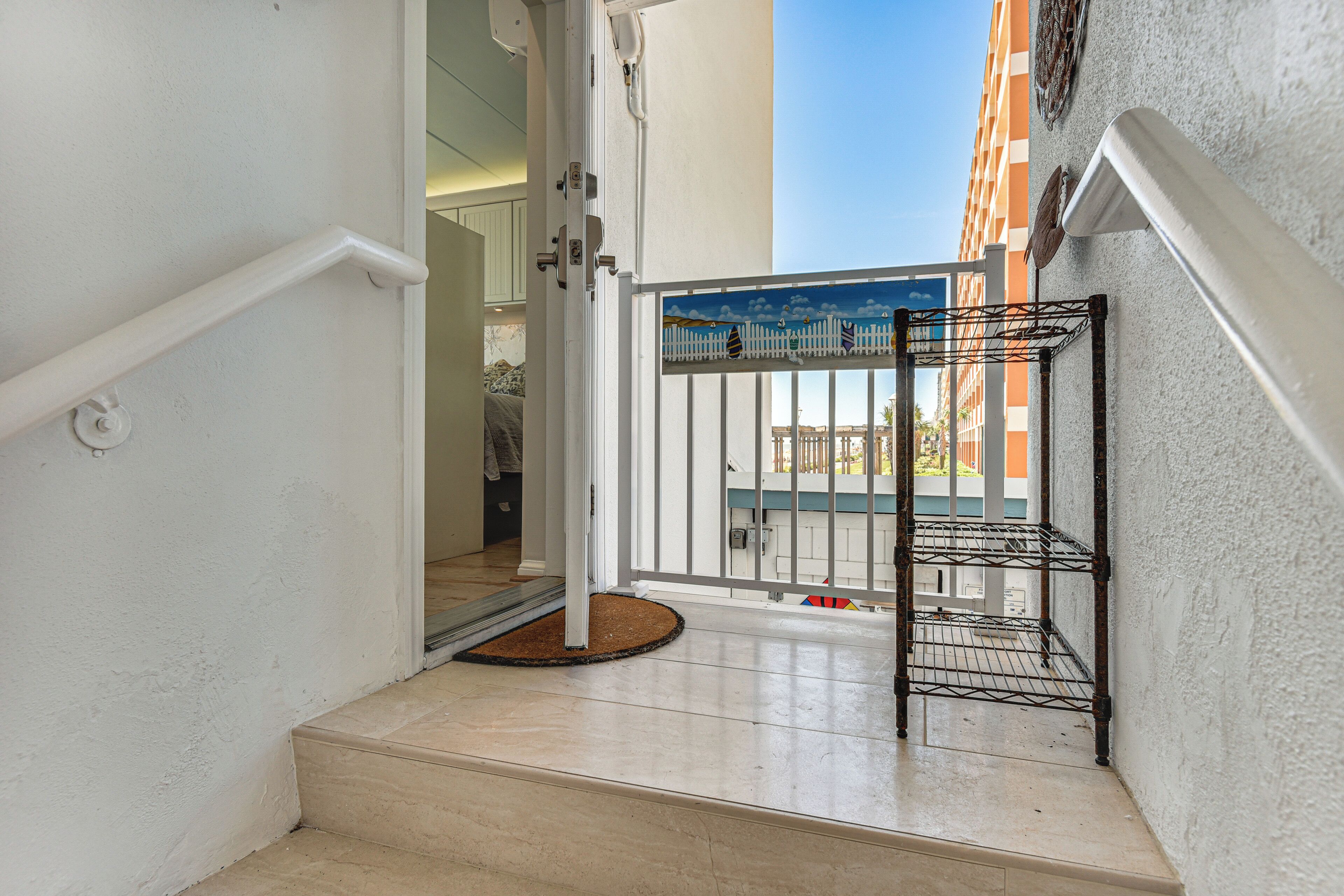 A staircase leading to a balcony with a metal rack, a white door, and a view of a building.