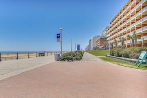 Um hotel à beira-mar com um caminho de tijolos vermelhos, palmeiras e um céu azul límpido.