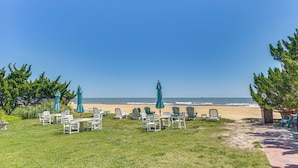 Una zona verda amb seients exteriors i ombrel·les, un camí que condueix a la platja, i una vista de l'oceà.