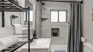 Een badkamer met een witte wastafel, een toilet, een douche met gordijn, een handdoekrek en een klein raam.