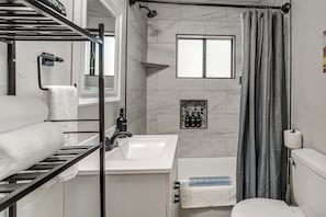 A bathroom with a white sink, a toilet, a shower with a curtain, a towel rack, and a small window. - Historic Prescott Gem! Walk to Whiskey Row! (Prescott)