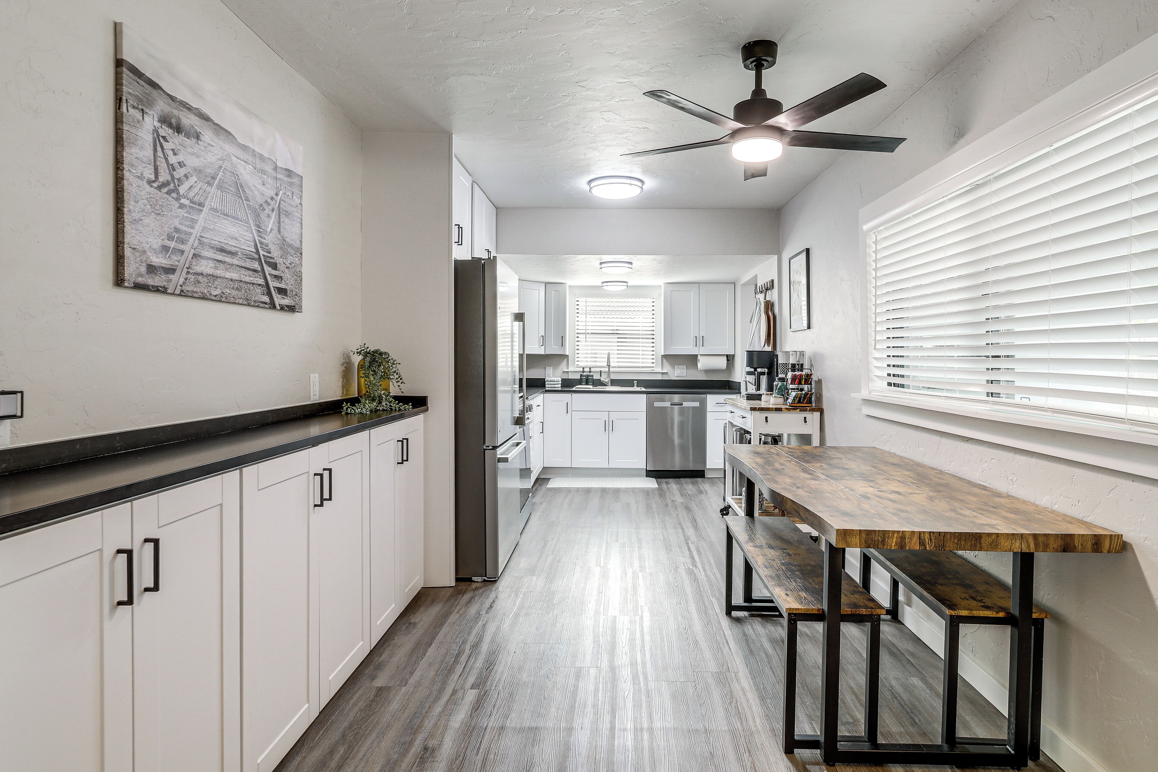 A kitchen with white cabinets, a wooden table, and a ceiling fan.