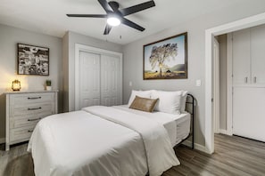 A bedroom with a bed, a ceiling fan, a dresser, a door, and a painting on the wall. - Historic Prescott Gem! Walk to Whiskey Row! (Prescott)