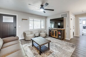 Sala de estar con sofá, mesa de centro, ventilador de techo y una zona de cocina con microondas y armarios.