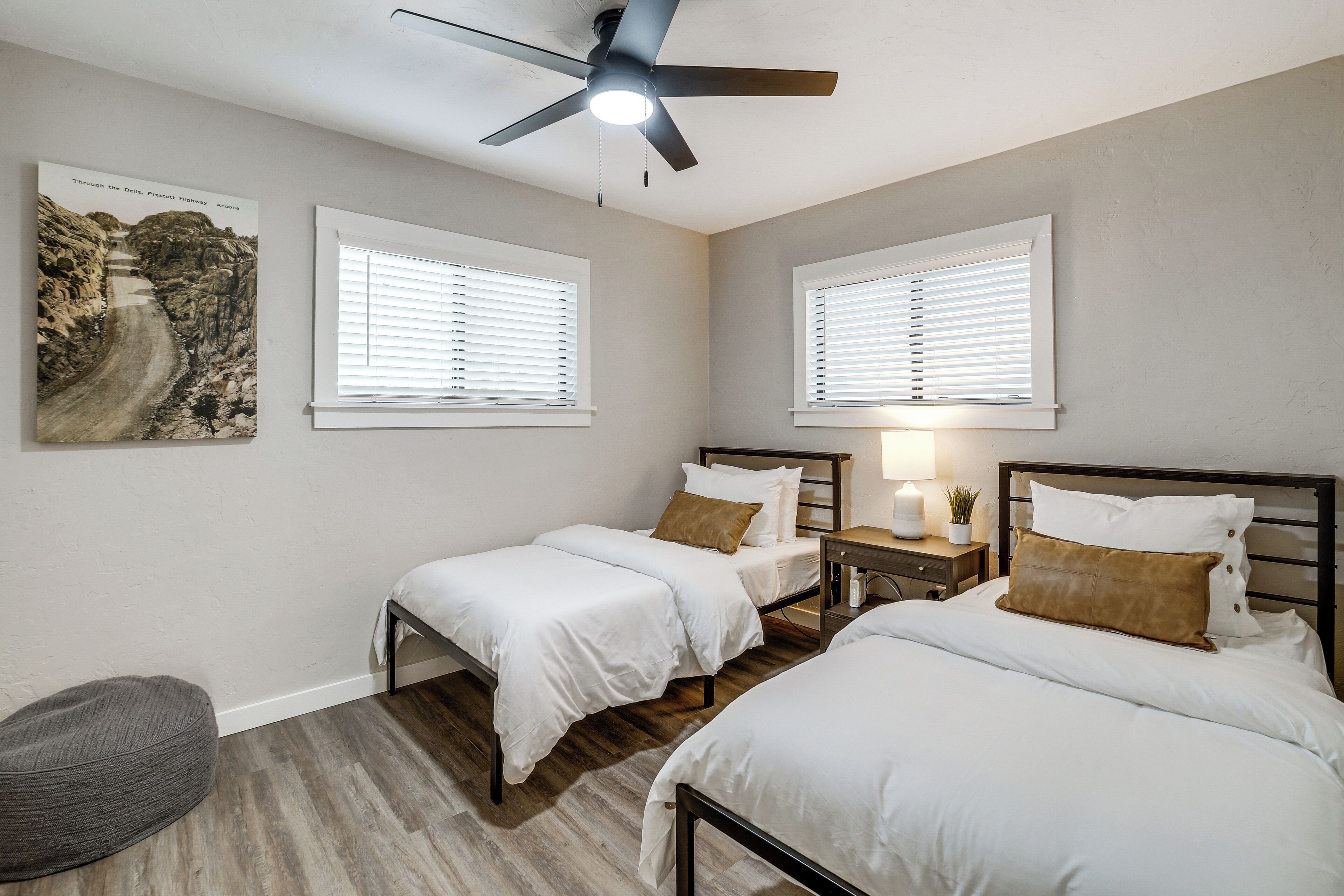 A bedroom with two beds, a ceiling fan, and two windows with blinds.