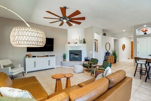 A living room with a fireplace, ceiling fan, and a television. - Saguaro Sanctuary: Tucson Home w/ Outdoor Oasis (Tucson)