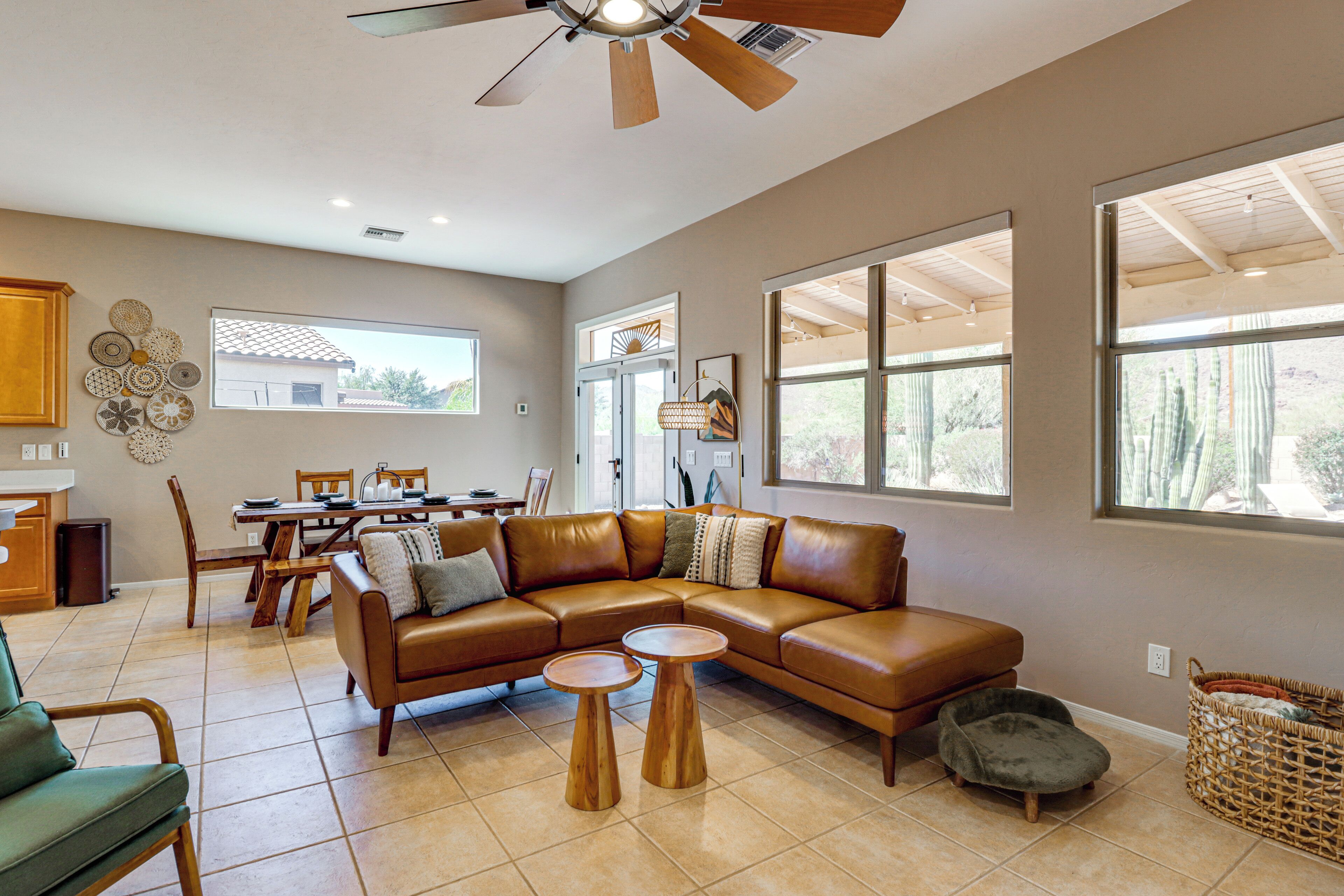 A spacious living room with a brown leather sectional sofa, two wooden side tables, and a dining area with wooden chairs and a table.