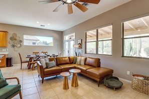 A spacious living room with a brown leather sectional sofa, two wooden side tables, and a dining area with wooden chairs and a table. - Saguaro Sanctuary: Tucson Home w/ Outdoor Oasis (Tucson)