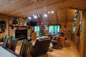 Ein gemütliches Cabin-Interieur mit Kamin aus Stein, einem Weihnachtsbaum, Holzmöbeln und einer Steinwand.