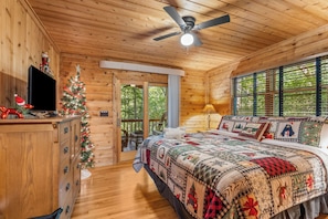 A cozy wooden cabin bedroom with a bed, a television, a Christmas tree, and a window with blinds. - The Christmas Cabin | Creekside Hot Tub Escape (Mineral Bluff)