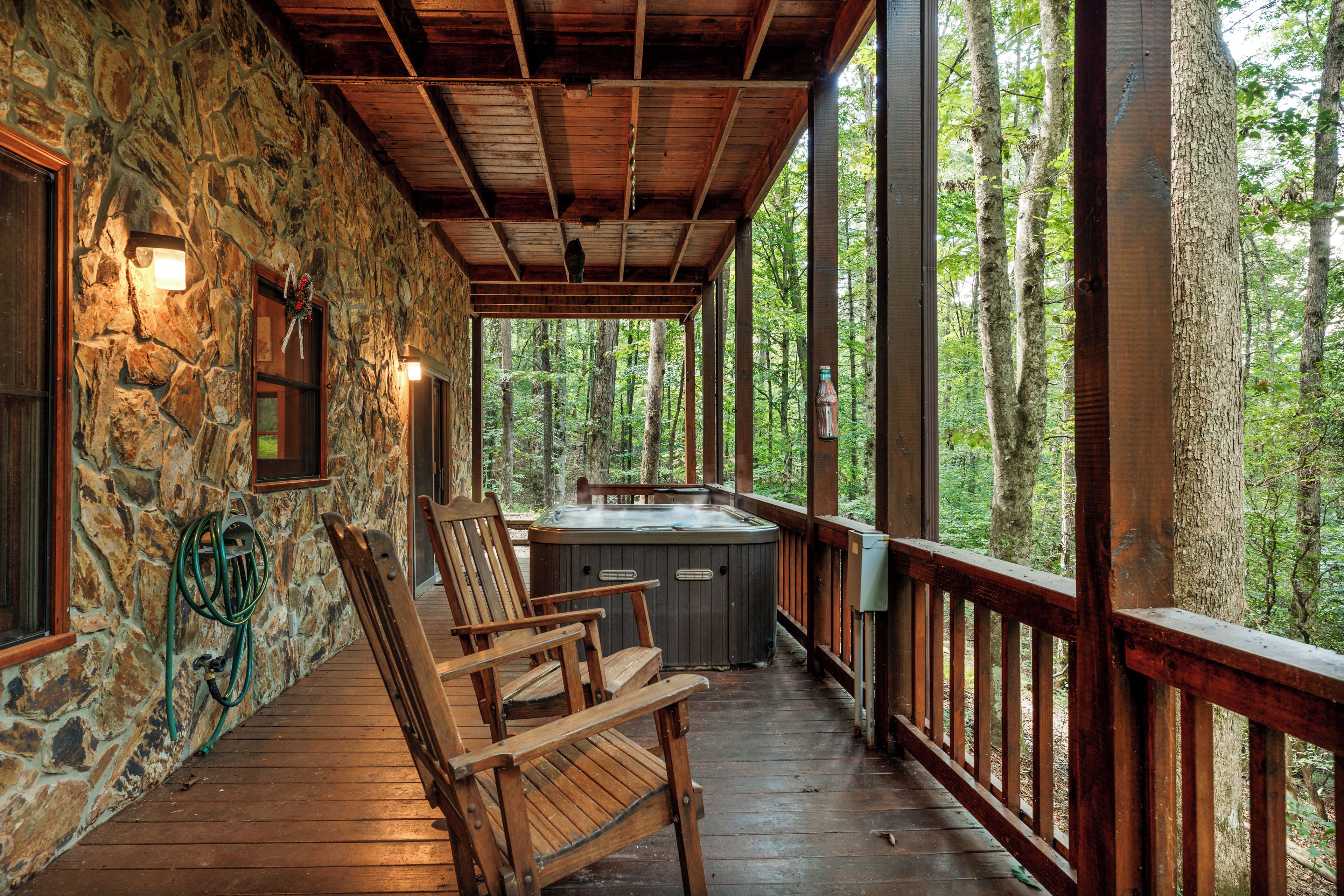 Una terraza de madera con paredes de piedra, un jacuzzi y sillas de madera.