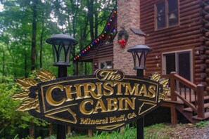 A sign for 'The Christmas Cabin' with a rustic cabin background. - The Christmas Cabin | Creekside Hot Tub Escape (Mineral Bluff)
