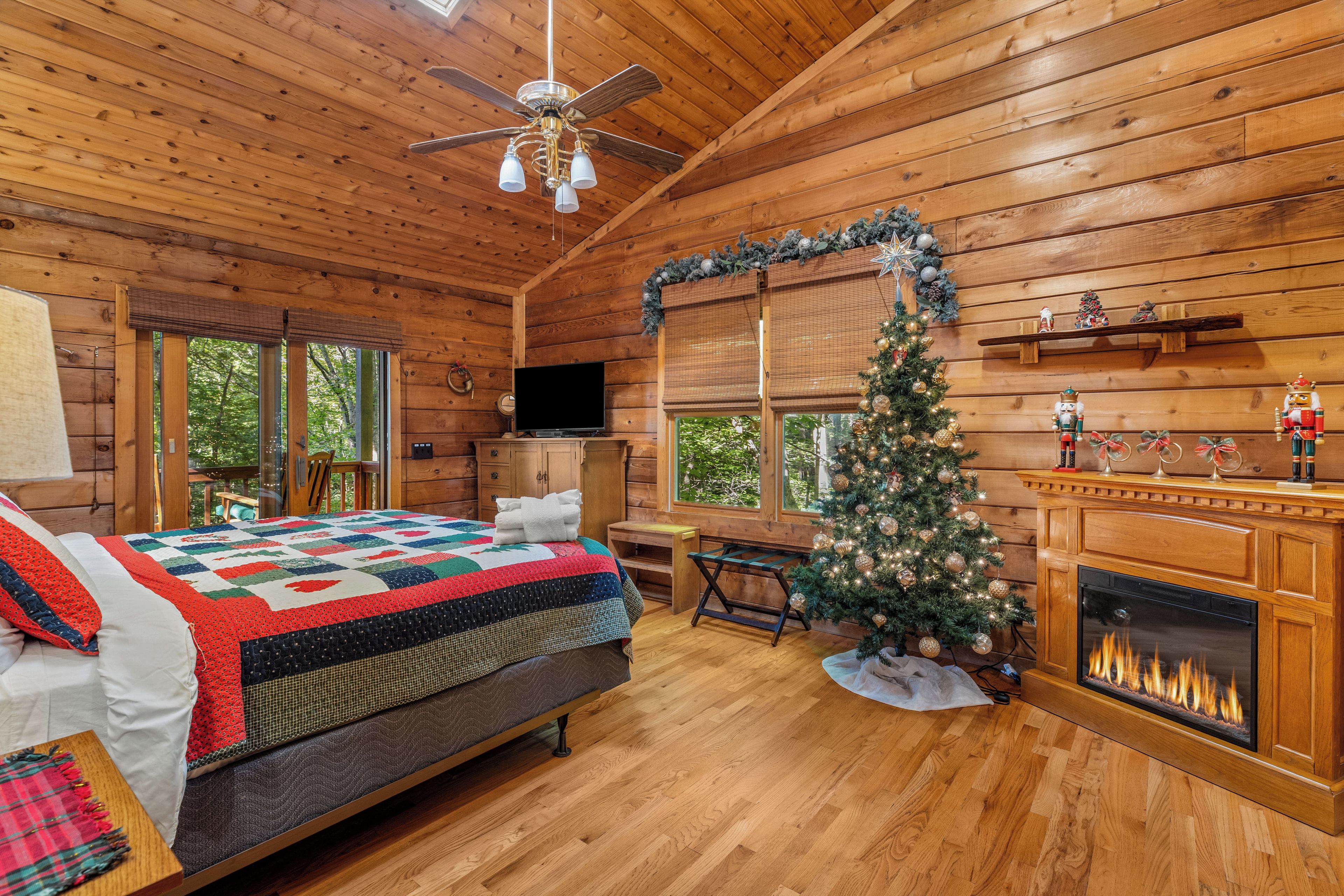 L’intérieur d’un chalet chaleureux, avec un plafond en bois, un lit recouvert d’une courtepointe, un téléviseur, un sapin de Noël et une cheminée.