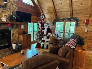 A cozy cabin interior with a fireplace, a Christmas tree, and a person in a Santa costume. - The Christmas Cabin | Creekside Hot Tub Escape (Mineral Bluff)