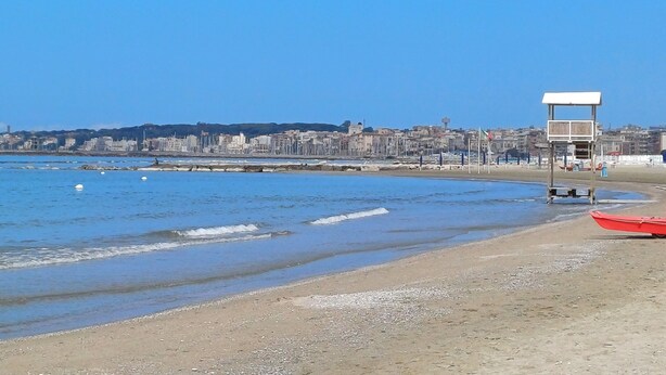 Una spiaggia con una torretta di salvataggio, acqua calma e uno skyline sullo sfondo.