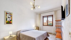 Una camera da letto con un letto, un comodino, una lampada, un'opera d'arte, una finestra e una TV appesa al muro.