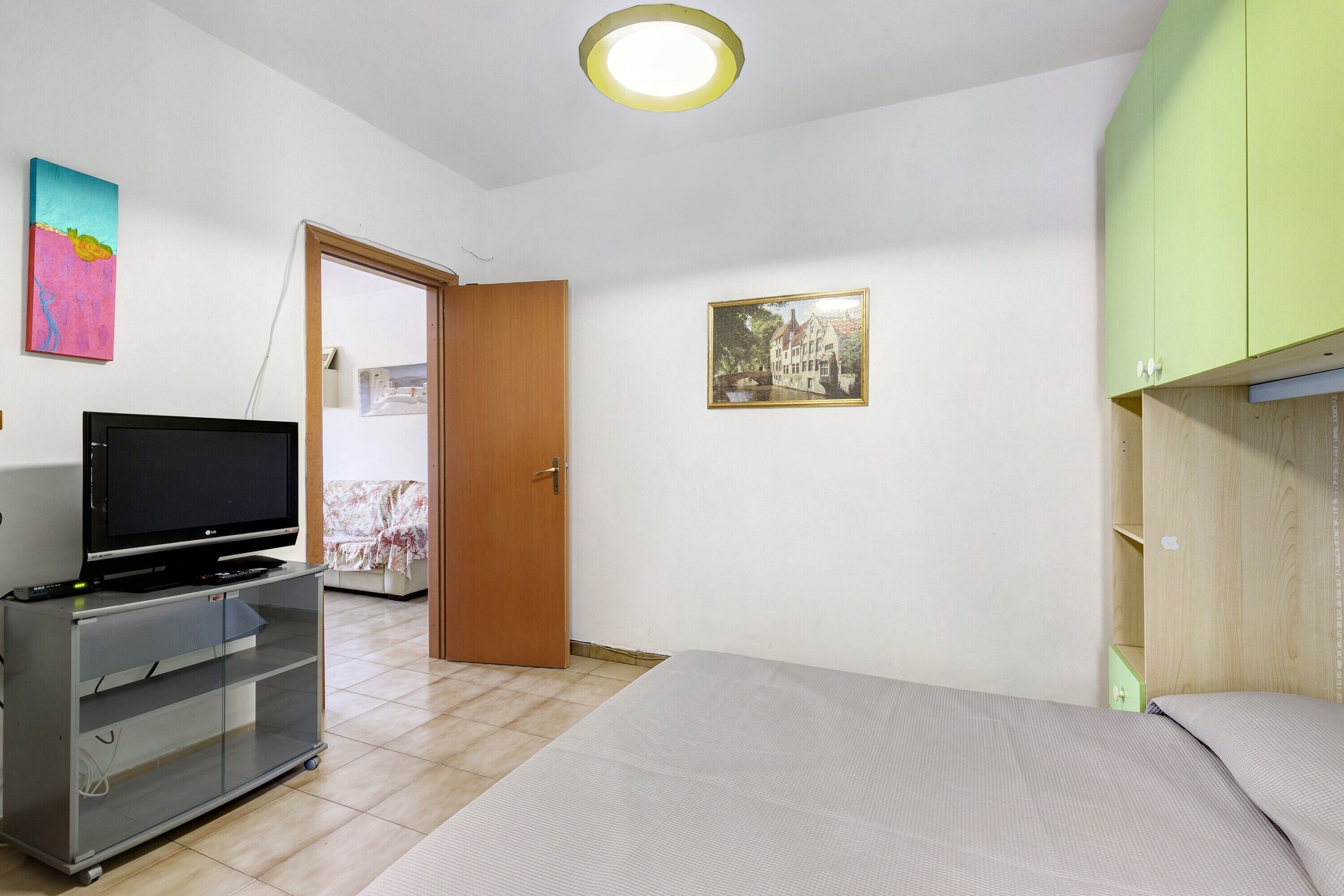 Une pièce avec un lit, un téléviseur posé sur un meuble, une porte et un tableau encadré au mur.