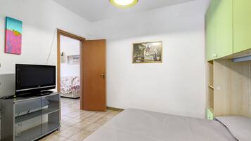 Une pièce avec un lit, un téléviseur posé sur un meuble, une porte et un tableau encadré au mur.