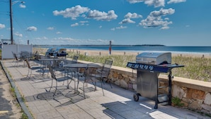 Un patio exterior con mesas y sillas, una parrilla y vistas a la playa y el océano.