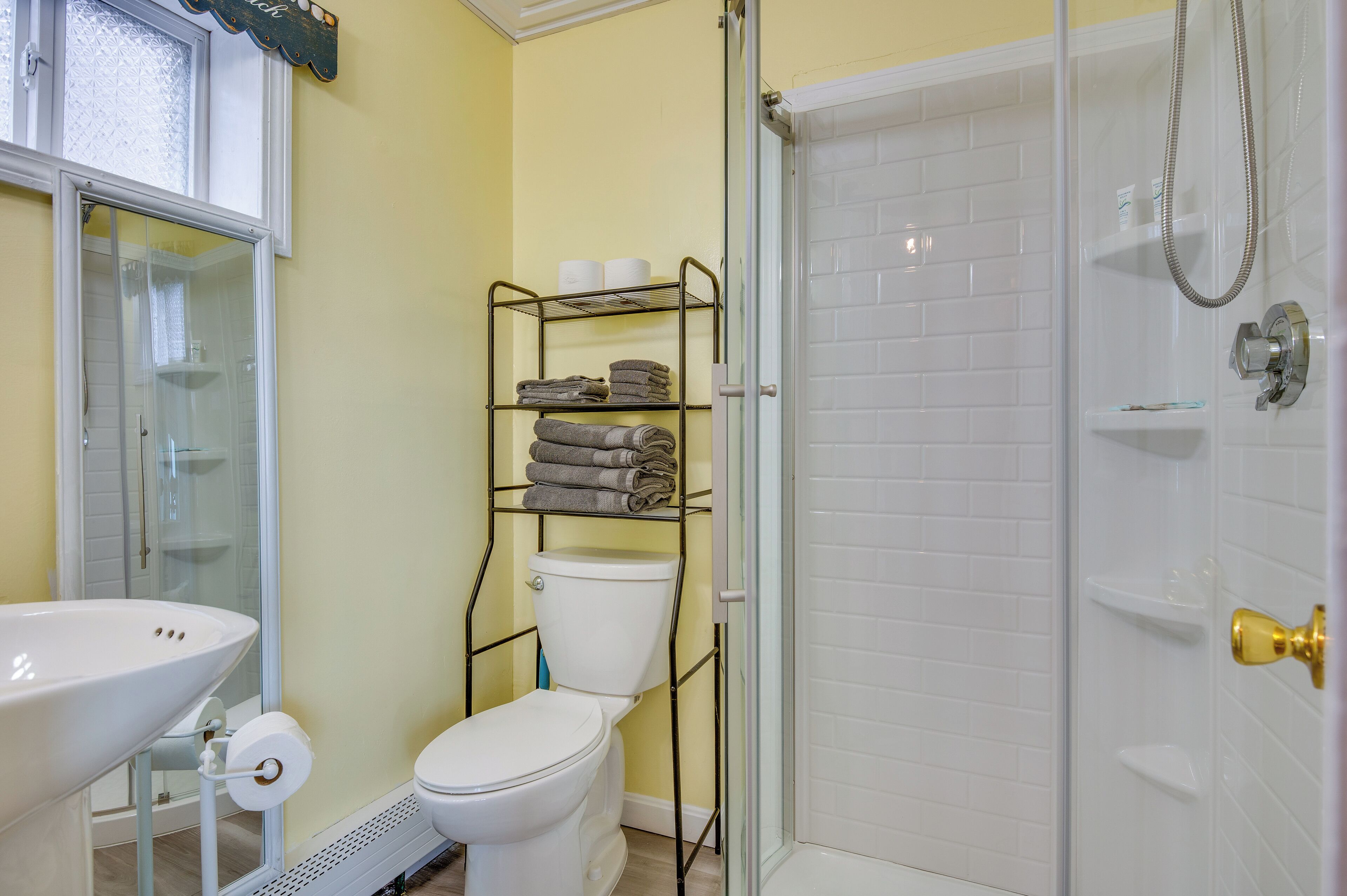 A bathroom with a toilet, a sink, a glass shower enclosure, and a metal towel rack with folded towels.