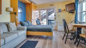 Una habitación con cama, sofá, mesa de comedor con sillas, televisión y una escalera que da a un espacio exterior.