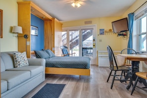 Ein Zimmer mit einem Bett, einer Couch, einem Esstisch mit Stühlen, einem Fernseher und einer Treppe, die zu einem Außenbereich führt.