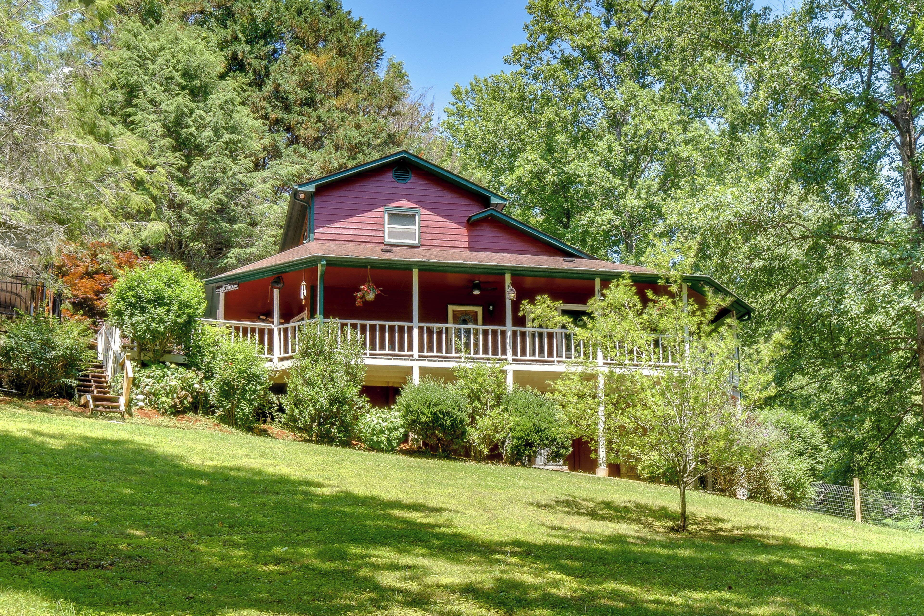 A red house with a porch, surrounded by trees and a grassy yard.