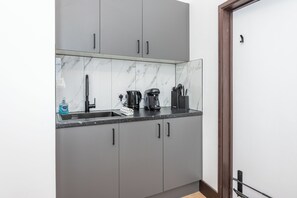 Eine Küche mit grauen Schränken, einer Marmor-Spritzschutzwand und einer Kaffeemaschine.