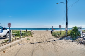 Uma trilha de areia leva ao oceano, com uma caminhonete branca estacionada ao lado.
