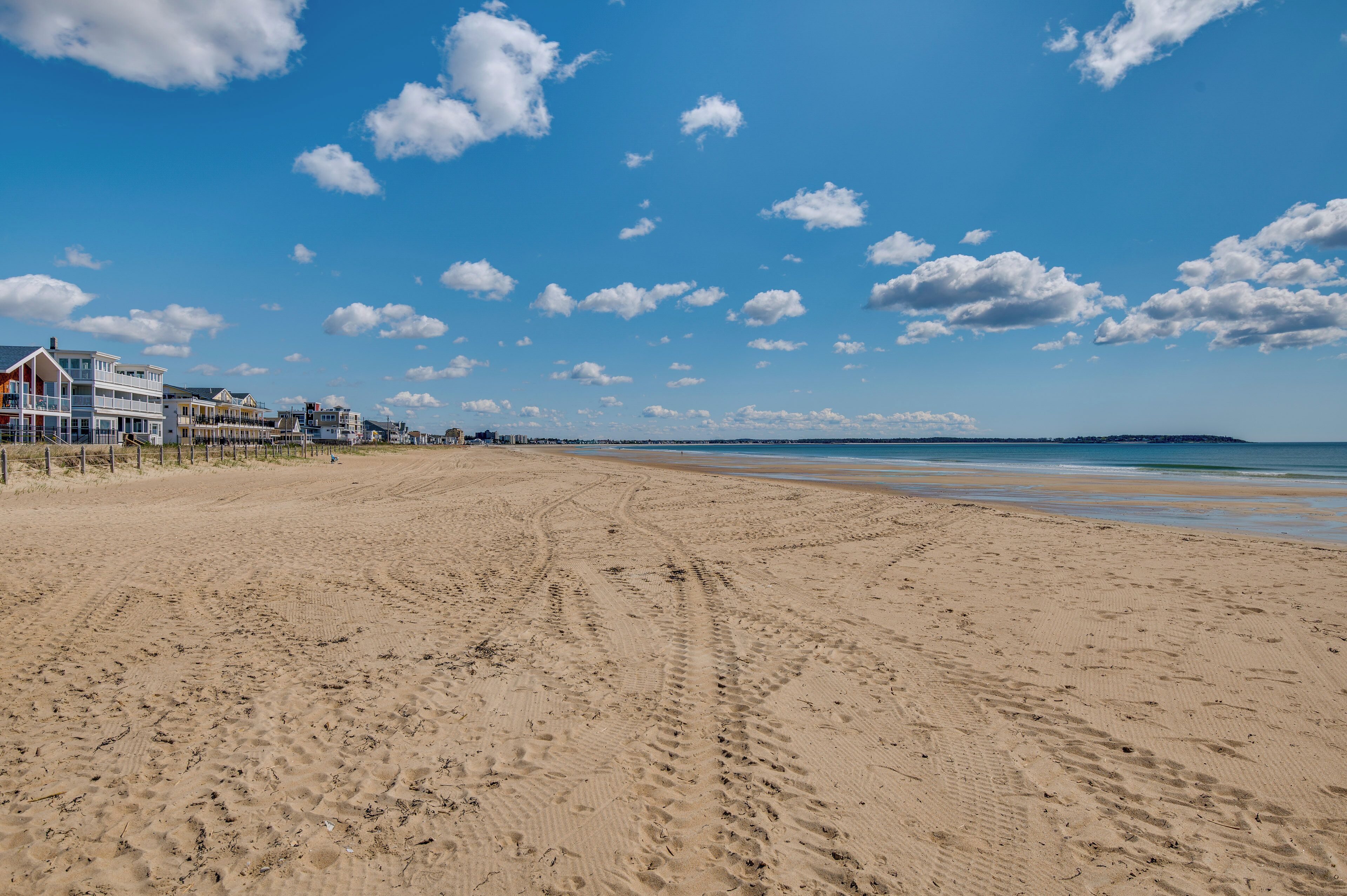 A wide sandy beach with footprints, a row of beach houses, and a clear blue sky.