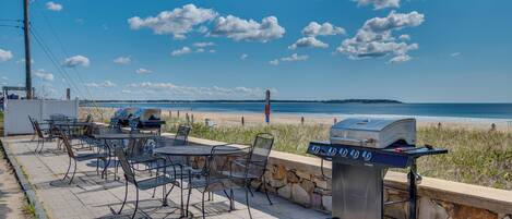 Eine Terrasse mit Sitzgelegenheit und Grill, mit Blick auf einen Strand.