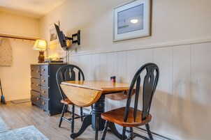 Un comedor con una mesa y sillas de madera, una lámpara, un televisor montado en la pared y un cuadro enmarcado.