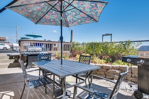 Um pátio externo com mesa, cadeiras, churrasqueira e um guarda-sol decorativo.