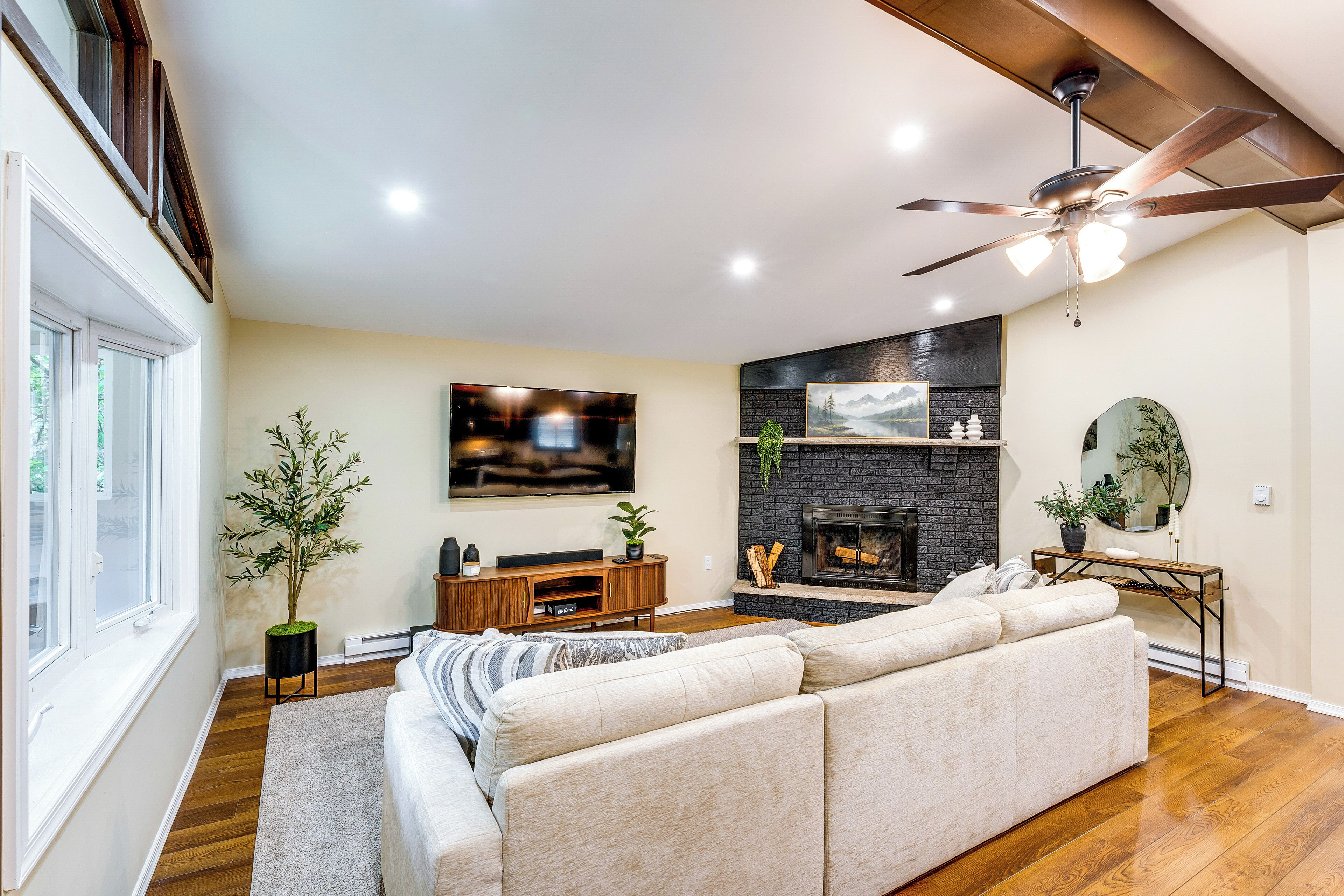 A living room with a sectional sofa, a flat-screen TV, a fireplace, and a ceiling fan.