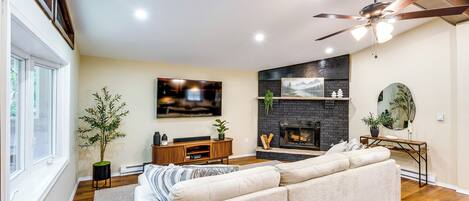A living room with a sectional sofa, a flat-screen TV, a fireplace, and a ceiling fan.