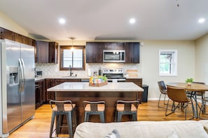 A modern kitchen with dark wood cabinets, stainless steel appliances, and a central island with bar stools. - Poconos Family Retreat w/ Fire Pit & Sunroom! (Tobyhanna)